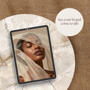 May include: A digital tablet displays a serene image of a person draped in sheer fabric. The tablet rests on a marble-like surface, with a burlap background. A circular graphic reads "See your brand come to life."