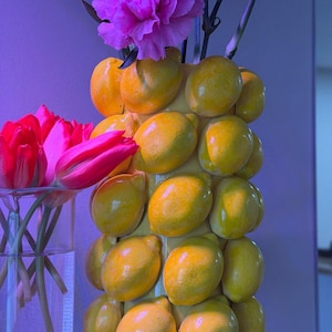 Könnte beinhalten: Eine gelbe Keramikvase mit zitronenförmigen Verzierungen, gefüllt mit leuchtend rosa Nelken und Tulpen. Die Vase ist ein einzigartiges Dekorationsobjekt, das jedem Innenraum einen Hauch von Verspieltheit verleiht.