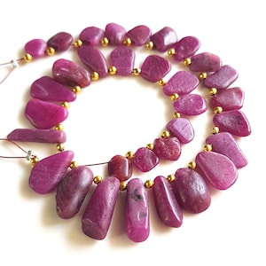 Peut inclure: Un collier de perles de rubis magenta irrégulières et polies, alternées avec de petites perles d'espacement rondes de couleur or métallique. Les perles sont enfilées sur un fil fin, formant un cercle avec des boucles visibles aux extrémités.