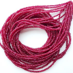 May include: A multi-strand necklace composed of numerous small, faceted, deep magenta-red gemstone beads. The strands are arranged in a circular, overlapping loop, showcasing the uniform size and reflective, textured surface of each individual bead.