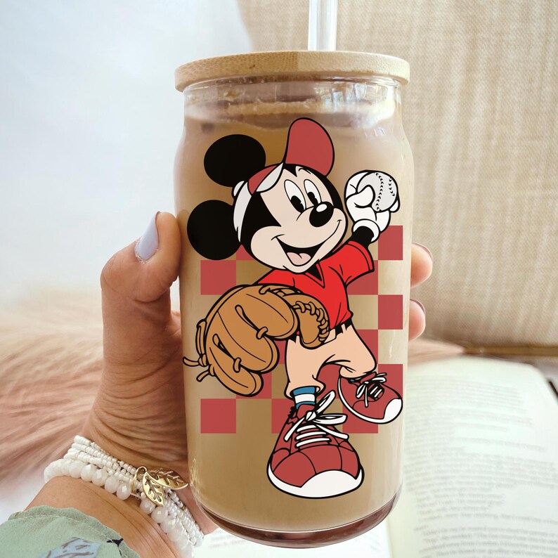 May include: A clear glass tumbler with a wooden lid and a straw, featuring a cartoon image of Mickey Mouse in a baseball uniform. The design includes a red and white checkered background.