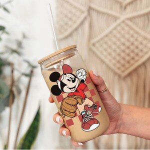May include: A clear glass tumbler with a wooden lid and a white straw. The tumbler features a cartoon image of Mickey Mouse in a baseball uniform. The background of the tumbler has a red and white checkered pattern.