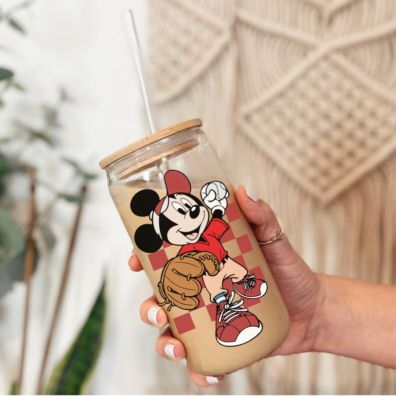 May include: A clear glass tumbler with a wooden lid and a white straw. The tumbler features a cartoon image of Mickey Mouse in a baseball uniform. The background of the tumbler has a red and white checkered pattern.