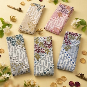 Könnte beinhalten: Fünf rechteckige Stoffstücke mit komplizierten Batikmustern in verschiedenen Farbpaletten, darunter Beige, Rosa, Blau und Grün. Jedes Stück zeigt detaillierte florale und geometrische Motive und ist auf einer hellen Oberfläche angeordnet.