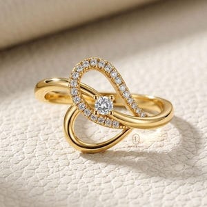 May include: A gold ring with a unique design. The ring features a central, round diamond and is accented with smaller diamonds along a curved, open setting. The band is a smooth, polished gold. The ring is displayed on a white surface.
