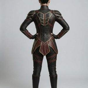 May include: A dark brown and black leather-like suit featuring structured shoulder armor, a quilted back panel, and a high collar. The garment includes layered hip panels, fitted sleeves with dark gloves, and matching tall boots with a sleek finish.