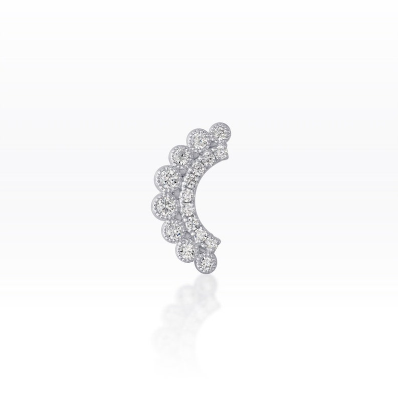 May include: A silver-coloured earring with a series of small, round, clear gemstones. The design features a crescent shape with a scalloped edge, creating a sparkling, elegant look. The earring is set against a white background.