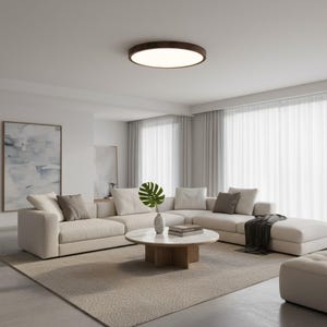 May include: A contemporary living room featuring a cream-coloured sectional sofa, a round coffee table, and a neutral-toned rug. A large painting adorns the wall, and sheer curtains filter the natural light. A dark brown, circular ceiling light illuminates the space.