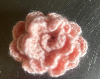 May include: A pink crocheted flower with a textured, ruffled design.