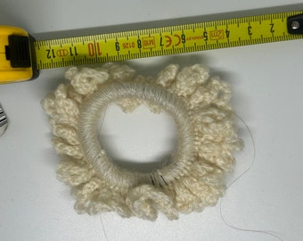 May include: A white crocheted hair scrunchie with a diameter of approximately 3 inches. The scrunchie is made of a soft, textured yarn and has a ruffled edge.