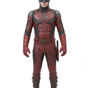 May include: A red and black superhero costume with a mask and horns. The costume features a large "D" emblem on the chest, a utility belt, and a holster. The gloves and boots are dark red.