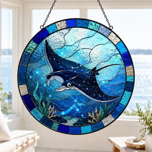 May include: Round stained glass window art featuring two manta rays swimming in a blue ocean scene. The artwork has a dark blue border and is suspended by a chain. The design includes aquatic plants and sparkling details.