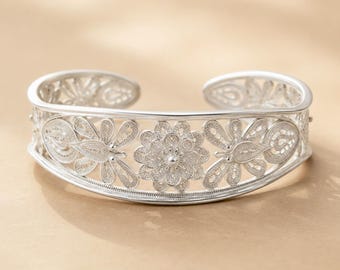 May include: A silver cuff bracelet featuring intricate filigree metalwork. The design displays a central floral motif flanked by two butterfly shapes on each side, all constructed from fine, delicate silver wire patterns in an openwork style.