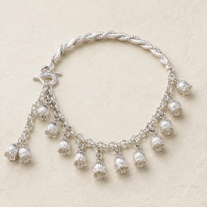 May include: A silver charm bracelet featuring a twisted metal band and a series of small, hanging bell-shaped flower charms. The bracelet includes a decorative S-hook clasp and multiple dangling floral pendants arranged along the chain links.