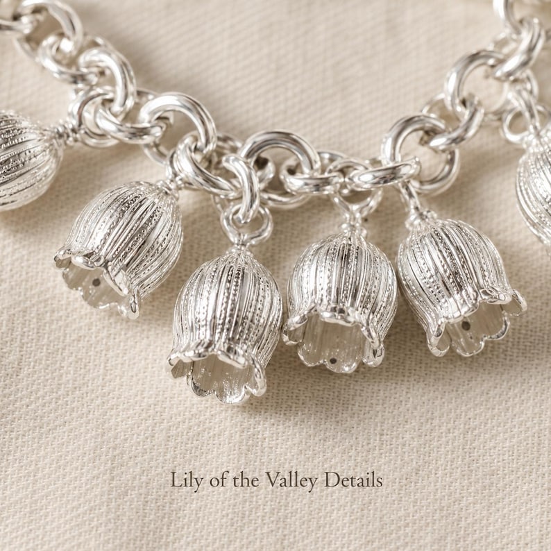 May include: A silver charm bracelet featuring multiple bell-shaped lily of the valley flower charms attached to a thick circular link chain. Each metallic flower charm displays vertical ribbed textures and scalloped edges. Text reads Lily of the Valley Details.