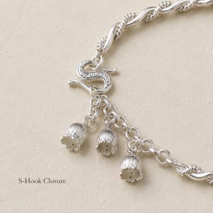 May include: A silver bracelet featuring a twisted metal chain and an S-hook closure. Three small, bell-shaped flower charms hang from the closure mechanism. The text S-Hook Closure is printed on the left side of the image near the clasp.