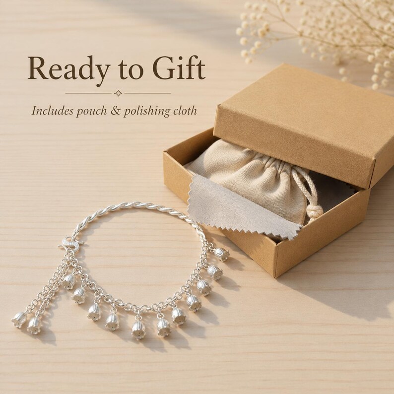 May include: A silver charm bracelet featuring multiple small bell-shaped pendants, accompanied by a beige drawstring pouch and a polishing cloth inside a brown cardboard gift box. The text Ready to Gift and Includes pouch & polishing cloth is visible.