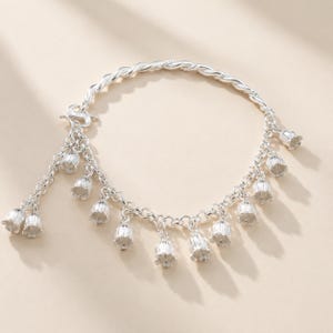 May include: A silver charm bracelet featuring a twisted chain and multiple dangling bell-shaped flower charms. The bracelet includes a secure clasp mechanism and a series of small, detailed floral pendants hanging evenly along the circular chain.
