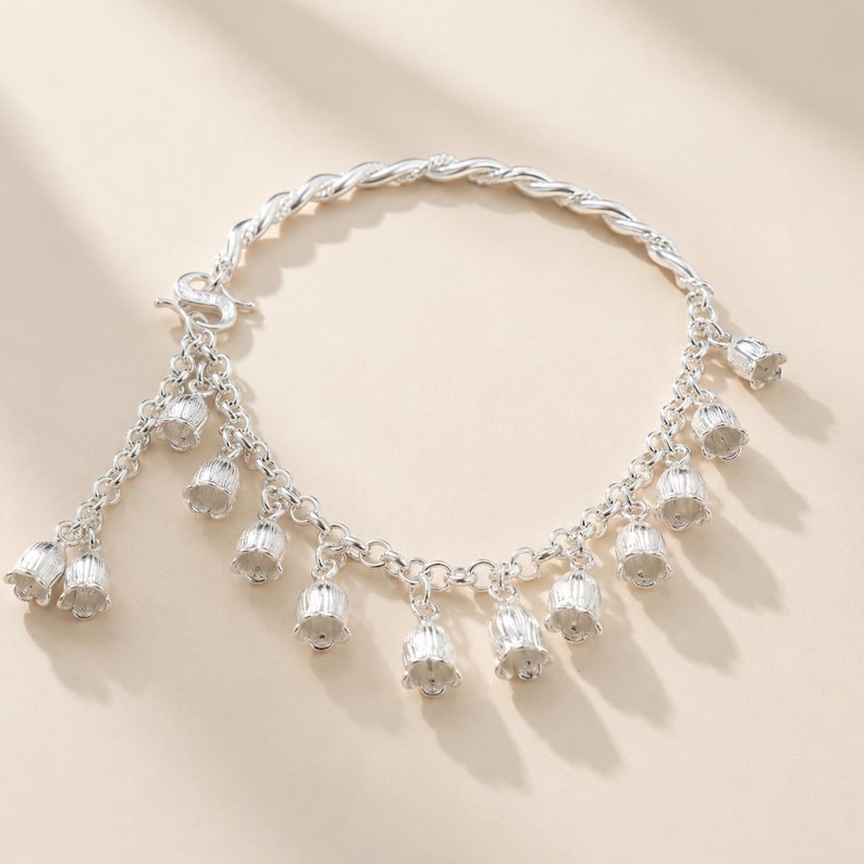 May include: A silver charm bracelet featuring a twisted chain and multiple dangling bell-shaped flower charms. The bracelet includes a secure clasp mechanism and a series of small, detailed floral pendants hanging evenly along the circular chain.