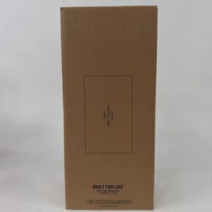 K&ouml;nnte beinhalten: Ein rechteckiger Versandkarton aus brauner Pappe mit einem schwarzen Rechteck in der Mitte, das den Text ATTACH SHIPPING LABEL HERE enth&auml;lt. Unten befindet sich der Text BUILT FOR LIFE LIFETIME WARRANTY und weitere kleine Schrift.