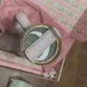 K&ouml;nnte beinhalten: Eine dekorative, runde Schmuckschatulle mit goldenem Rand und hellrosa Deckel. Die Schatulle ist ge&ouml;ffnet und zeigt einen hellrosa Schal und einen kleinen, runden Gegenstand im Inneren. Die Schatulle befindet sich in einer gr&ouml;&szlig;eren, gemusterten Schachtel.
