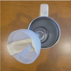 May include: A top-down view of a white tumbler with a matching lid and a clear straw. The tumbler features a white handle attached to the side, and the interior is metallic silver. The lid is partially detached, revealing the open circular top.