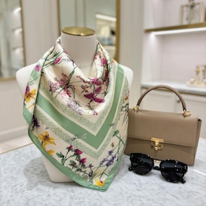 May include: A square silk scarf featuring a floral design in pink, yellow, and purple, with green borders and dragonfly details. A tan handbag and black sunglasses are also present.