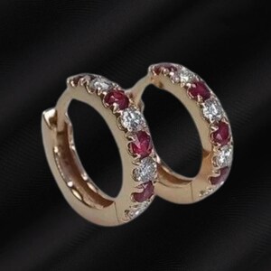May include: A pair of hoop earrings crafted from rose gold, featuring an alternating pattern of round-cut red rubies and clear white diamonds set along the front-facing outer edge of each circular hoop, secured with a hinged closure mechanism.