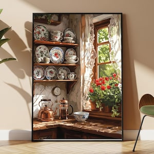 Op de afbeelding: Een ingelijste muurkunstprint met een keukenscène met houten planken vol borden en kopjes met bloemmotieven. Daaronder staan een koperen waterkoker, een cafetière en een kom op een aanrecht bij een raam met rode bloemen en kanten gordijnen.