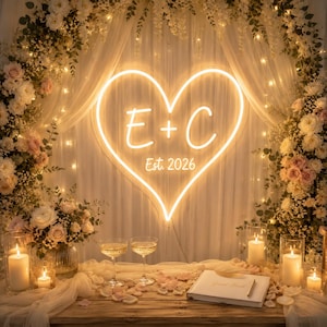May include: A romantic wedding scene with a glowing heart-shaped neon sign featuring the letters "E + C" and "Est. 2026". The scene includes champagne glasses, candles, flowers, and a guest book, creating a warm and inviting atmosphere.