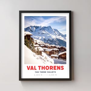 Könnte beinhalten: Gerahmter Druck mit einer verschneiten Bergdorf-Szene unter blauem Himmel. Der Druck enthält den Text "VAL THORENS" in Rot, darunter "THE THREE VALLEYS" und Höhenangaben: 2.300 m → 3.230 m. Das Kunstwerk ist in einem schwarzen Rahmen.
