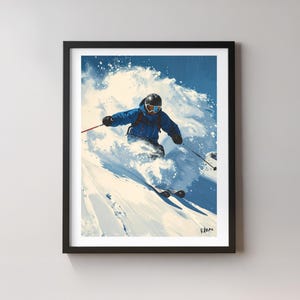 Op de afbeelding: Ingelijste kunstdruk van een skiër in een blauwe jas die een besneeuwde berg afdaalt. Het kunstwerk toont de actie en beweging van de skiër. De print zit in een zwarte lijst.