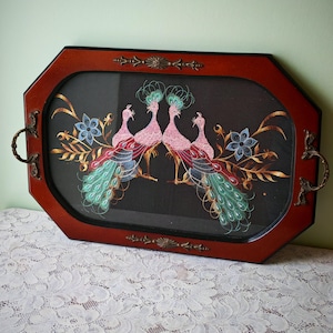 Peut inclure: Un plateau de service octogonal avec un cadre en bois rouge foncé et des poignées en métal couleur bronze ornementées. Le centre présente un panneau noir décoré d'une broderie complexe de deux paons roses entourés de fleurs bleues et de feuillage doré.