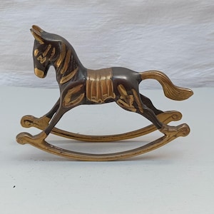 Könnte beinhalten: Eine Schaukelpferd-Figur aus Messing mit dunkelbrauner Patina und polierten goldfarbenen Akzenten an Mähne, Schweif, Sattel und den geschwungenen Kufen. Das Metallpferd ist in einer Galoppbewegung dargestellt, wobei der Kopf leicht gesenkt ist.