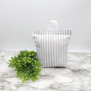 May include: A white doorstop with a blue and white striped fabric cover and a white fabric handle.
