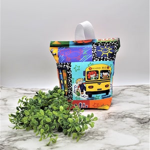 May include: A colorful fabric bag with a white handle. The bag has a school bus, children, and the words "School Bus" and "Rules" printed on it.