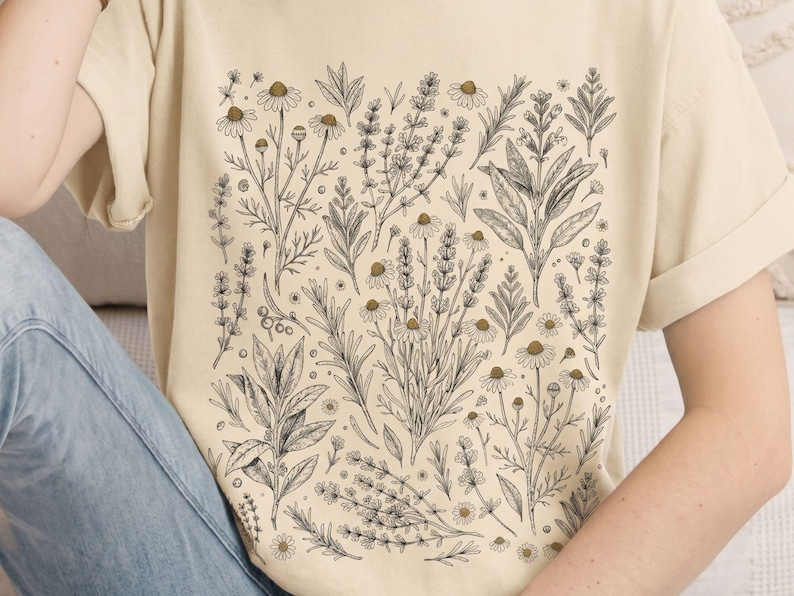 Soft Ivory cotton tee with a Victorian botanical scatter of kitchen herbs in dark charcoal ink, worn against pale denim — Scattered Kitchen Herbs Comfort Colors shirt for cottagecore witches and herb gardeners. By MythicThreadMagic.