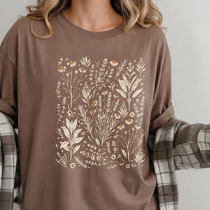 Rich Espresso brown garment-dyed tee with cream Victorian herbalist illustration, paired with a flannel and natural denim — Scattered Kitchen Herbs shirt for foraging-loving woodland aesthetes. By MythicThreadMagic.