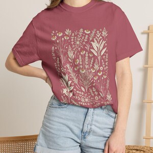 Warm Crimson red garment-dyed tee with cream Scattered Kitchen Herbs Victorian illustration, paired with high-waisted denim shorts in a soft natural light — bold cottagecore staple for witchy gardeners. By MythicThreadMagic.
