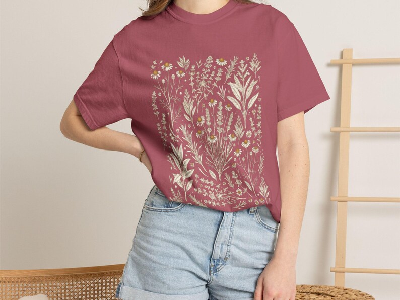 Warm Crimson red garment-dyed tee with cream Scattered Kitchen Herbs Victorian illustration, paired with high-waisted denim shorts in a soft natural light — bold cottagecore staple for witchy gardeners. By MythicThreadMagic.