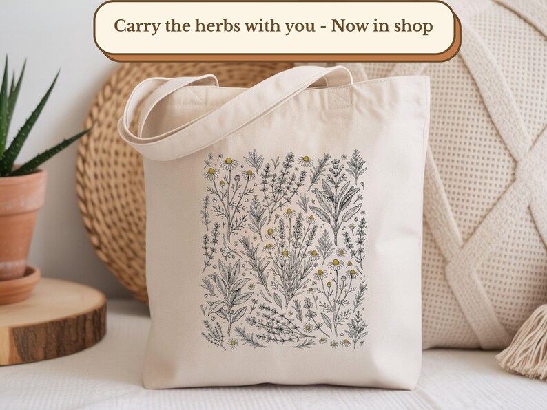 A cream-colored canvas tote bag featuring a detailed black and white botanical illustration of various herbs, including chamomile, lavender, rosemary, and sage, with subtle hints of yellow. The tote is displayed in a cozy, neutral-toned setting with a potted aloe vera plant, woven mats, and a textured pillow. A banner at the top reads, "Carry the herbs with you - Now in shop.