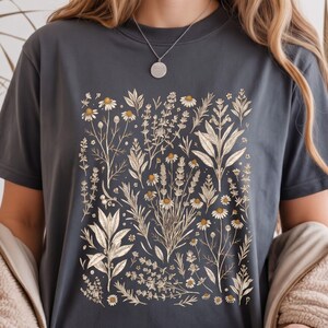 Moody dark Pepper Comfort Colors tee with cream Victorian herb illustration centered on the chest, paired with a soft cardigan in a cozy reading nook — Scattered Kitchen Herbs shirt for witchy herbalists and slow living lovers. By MythicThreadMagic.