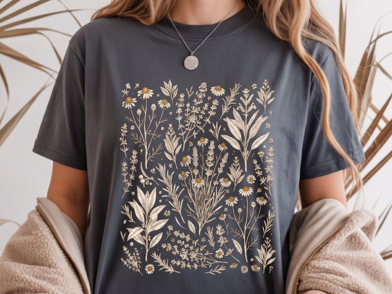 Moody dark Pepper Comfort Colors tee with cream Victorian herb illustration centered on the chest, paired with a soft cardigan in a cozy reading nook — Scattered Kitchen Herbs shirt for witchy herbalists and slow living lovers. By MythicThreadMagic.