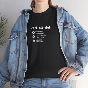 May include: Black t-shirt with the text "ctrl+alt+del" and the phrases "Control Yourself", "Alter Your Thinking", and "Delete Negativity" in white. The shirt is worn with a denim jacket.