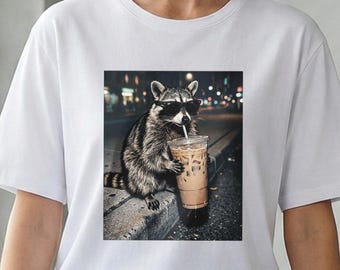 サングラスをかけたクールなアライグマが夜の街でアイスコーヒーを飲んでいる、面白いレトロな雰囲気の動物グラフィックTシャツ、アイスミルクティー好きのためのTシャツ