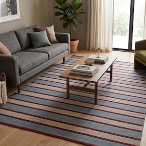 May include: A rectangular area rug with horizontal stripes in light blue, beige, and burgundy. The rug is placed on a hardwood floor in a living room setting, with a gray sofa, coffee table, and a green plant in the background.