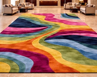 May include: A large, colorful area rug with a wavy, abstract design. The rug features vibrant bands of color, including yellow, orange, pink, blue, and green. The rug is placed in a well-lit, elegant room with neutral-toned furniture.
