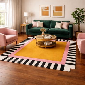 Pode incluir: Uma sala de estar com um tapete amarelo mostarda, uma borda rosa e uma borda listrada em preto e branco. O quarto inclui um sofá verde, duas poltronas rosa e uma mesa de centro redonda. O tapete mede aproximadamente 244 cm x 305 cm.
