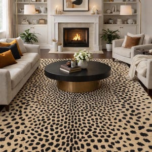 May include: A living room featuring a cheetah print rug, a black coffee table with a gold base, and a fireplace. Two beige sofas and two armchairs are arranged around the coffee table. The room has white walls and built-in shelves.