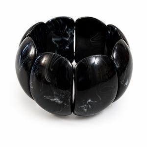 Peut inclure: Un bracelet noir et blanc marbré. Le bracelet est composé de grands segments arrondis, chacun avec une finition brillante. Les segments sont reliés pour former une forme large et circulaire. Le marbrage noir et blanc crée un motif unique.